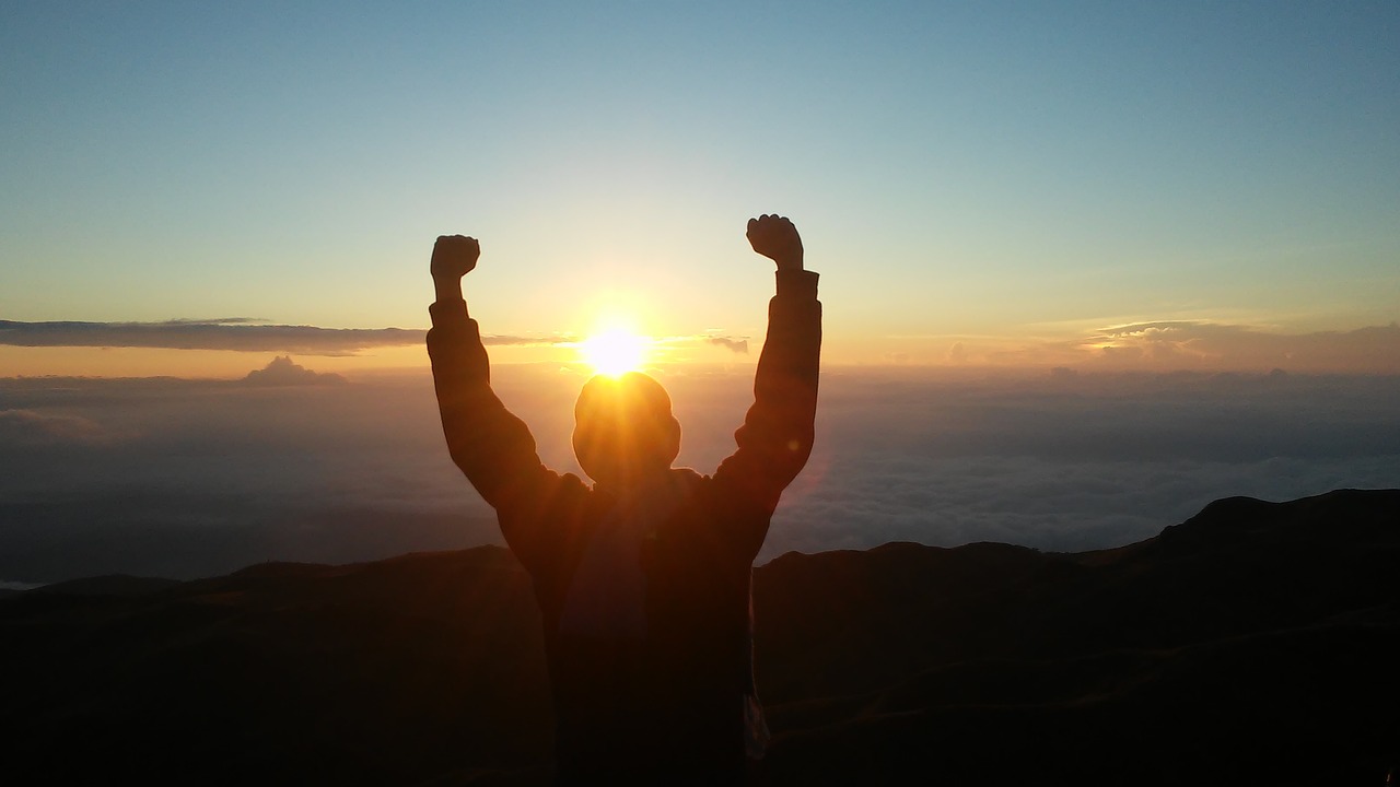 A person with their arms raised facing the sunrise.